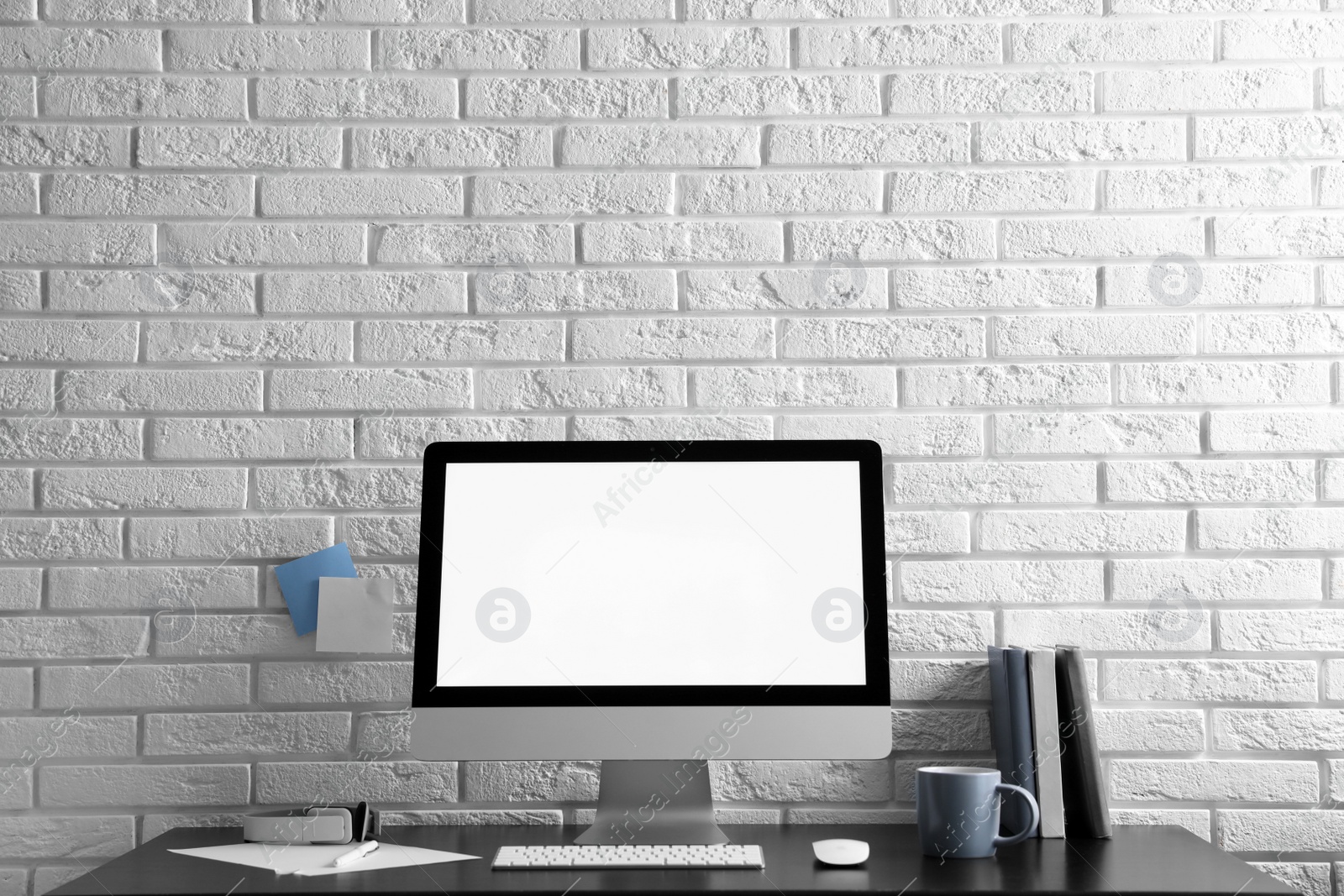 Photo of Comfortable workplace with modern computer on black table near white brick wall. Space for text