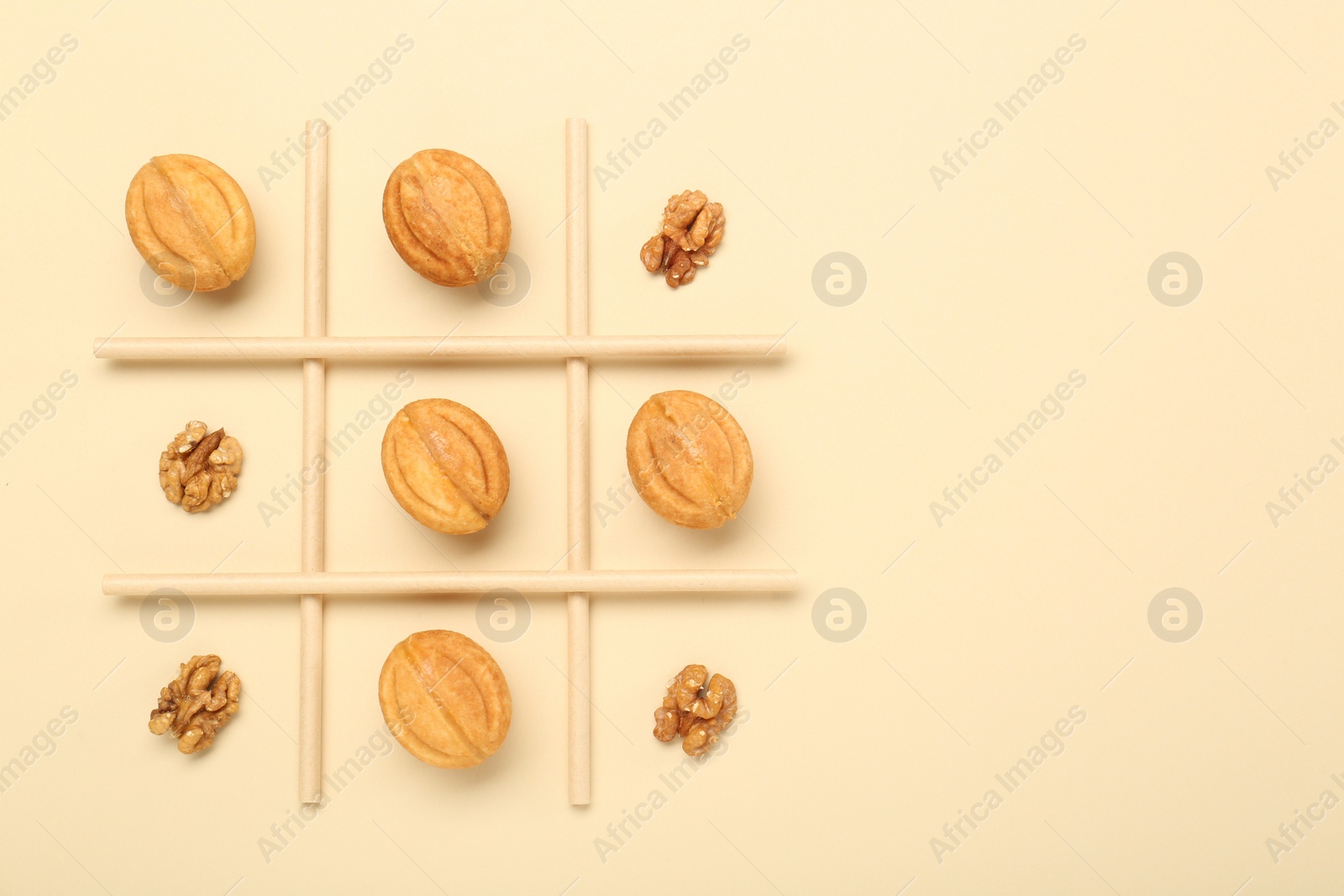 Photo of Tic tac toe game made with walnuts and cookies on beige background, top view. Space for text