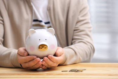 Photo of Man with piggy bank at wooden table, closeup