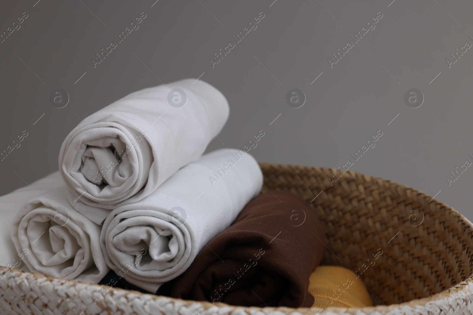 Photo of Different rolled shirts in basket against grey background, space for text. Organizing clothes
