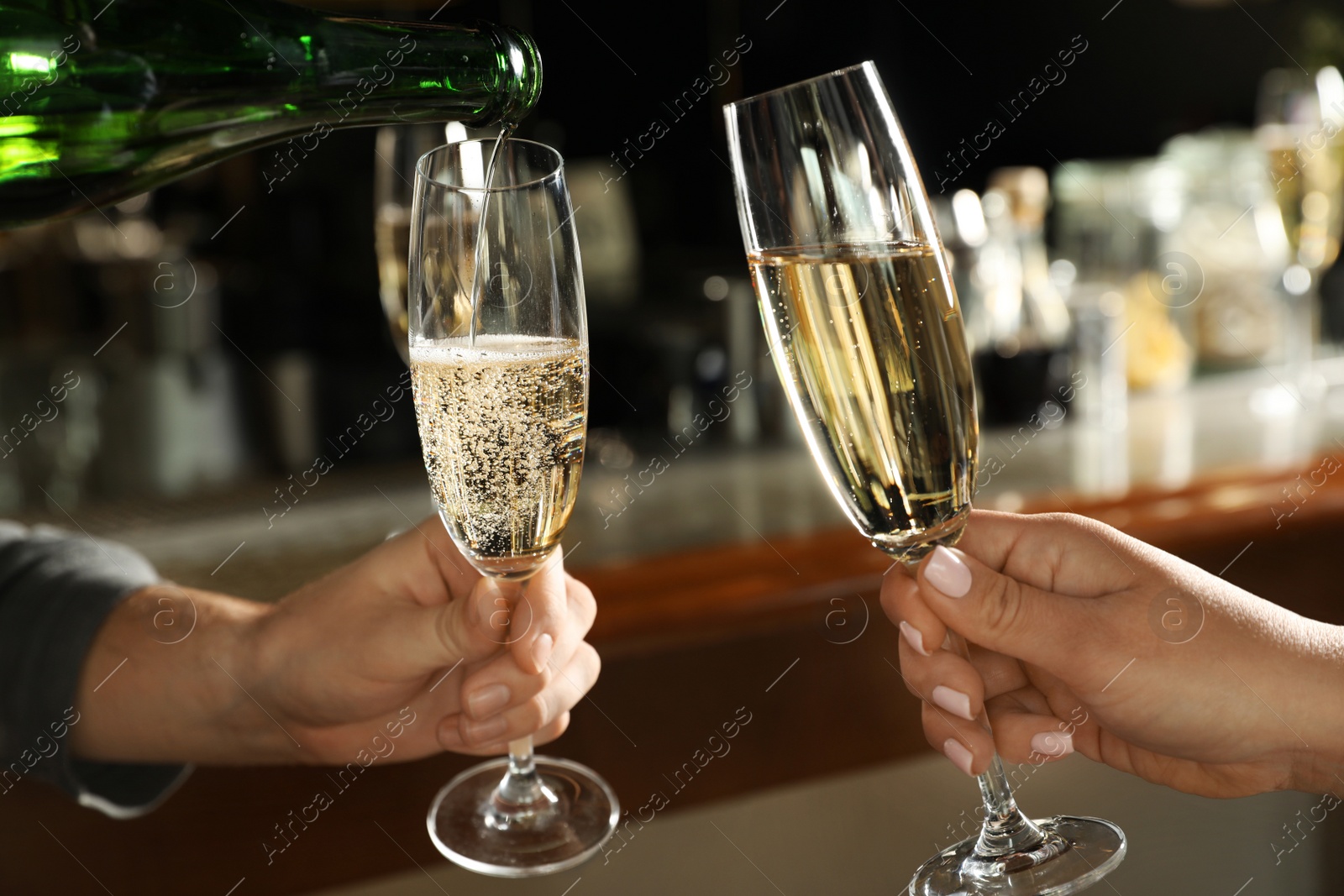 Photo of Pouring champagne from bottle for couple in bar, closeup