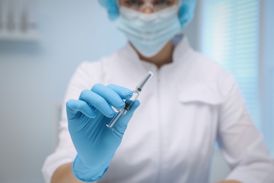 Doctor holding syringe with COVID-19 vaccine on blurred background, closeup