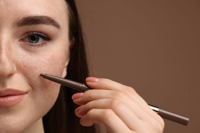 Beautiful woman drawing freckles with pen on brown background, closeup