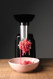 Electric meat grinder with beef mince on wooden table against grey background