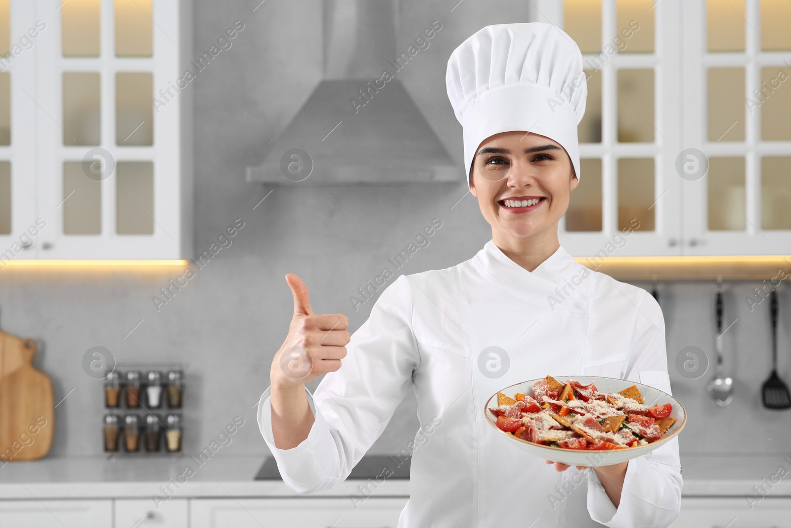 Photo of Portrait of professional chef presenting delicious dish and showing thumb up in kitchen. Space for text