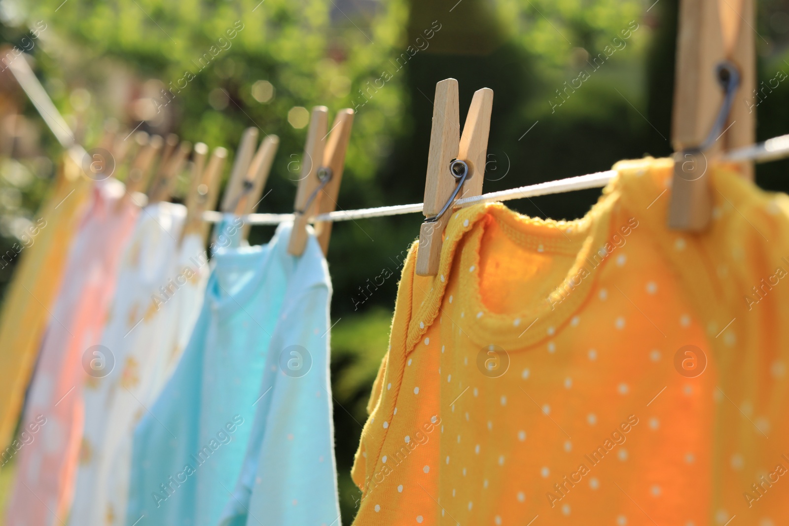 Photo of Clean baby onesies hanging on washing line in garden, closeup. Drying clothes