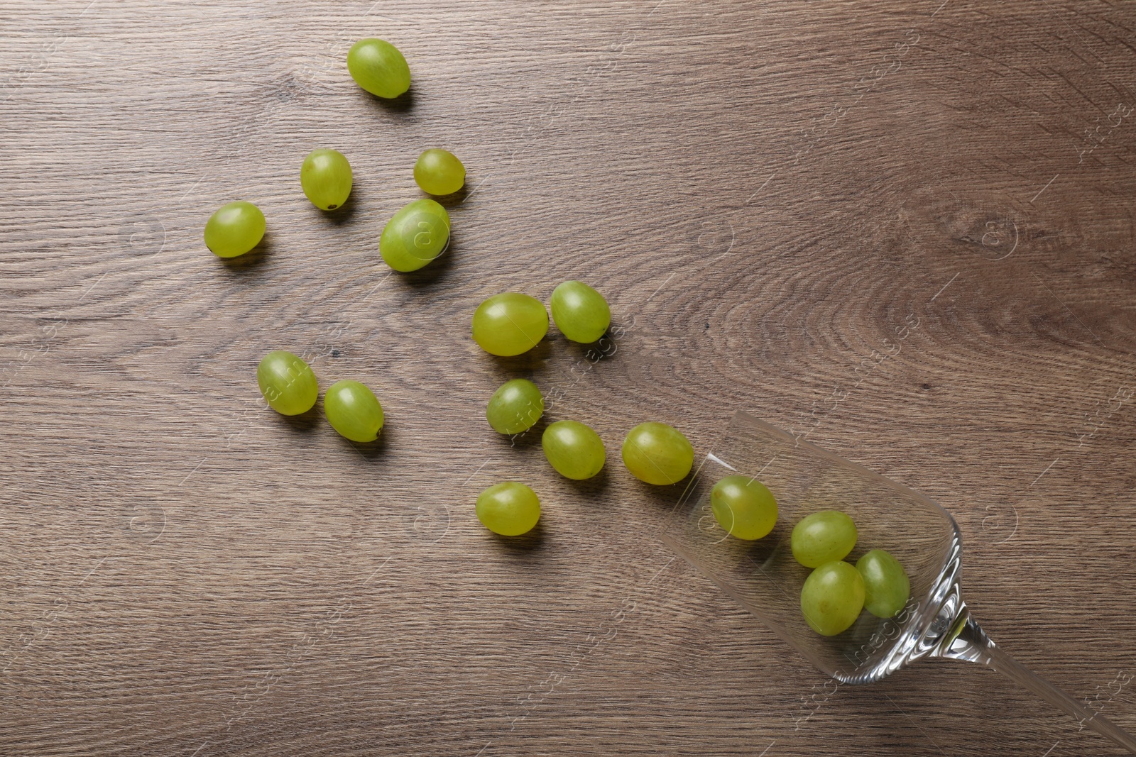 Photo of Wineglass with scattered grapes on wooden table, flat lay