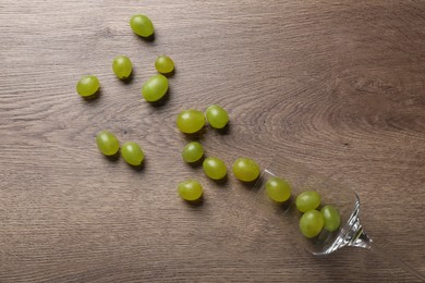 Wineglass with scattered grapes on wooden table, flat lay