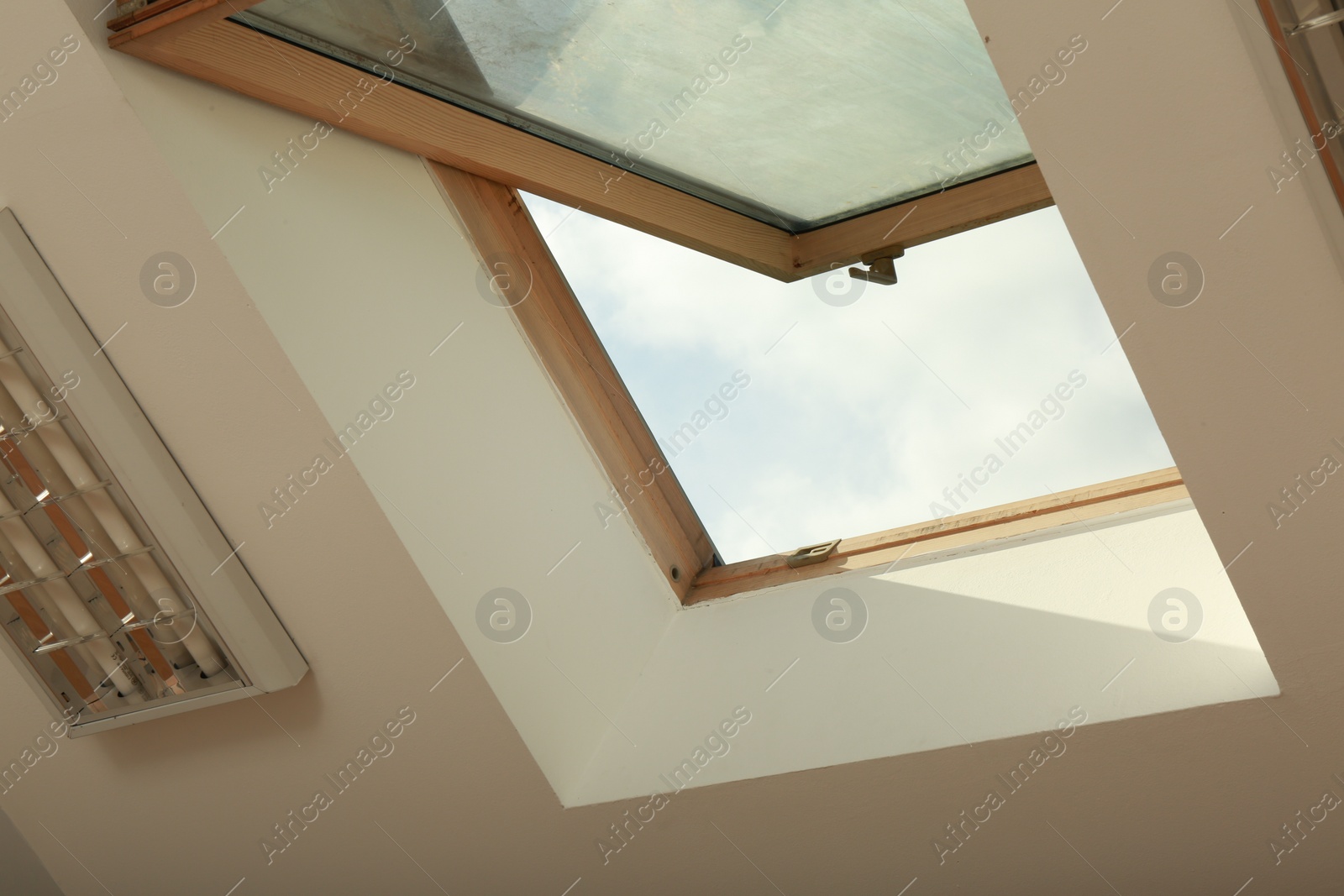 Photo of Open skylight roof window on slanted ceiling in attic room, low angle view