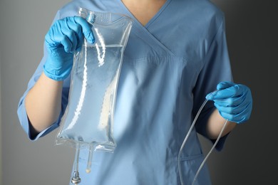 Nurse with IV infusion set on grey background, closeup