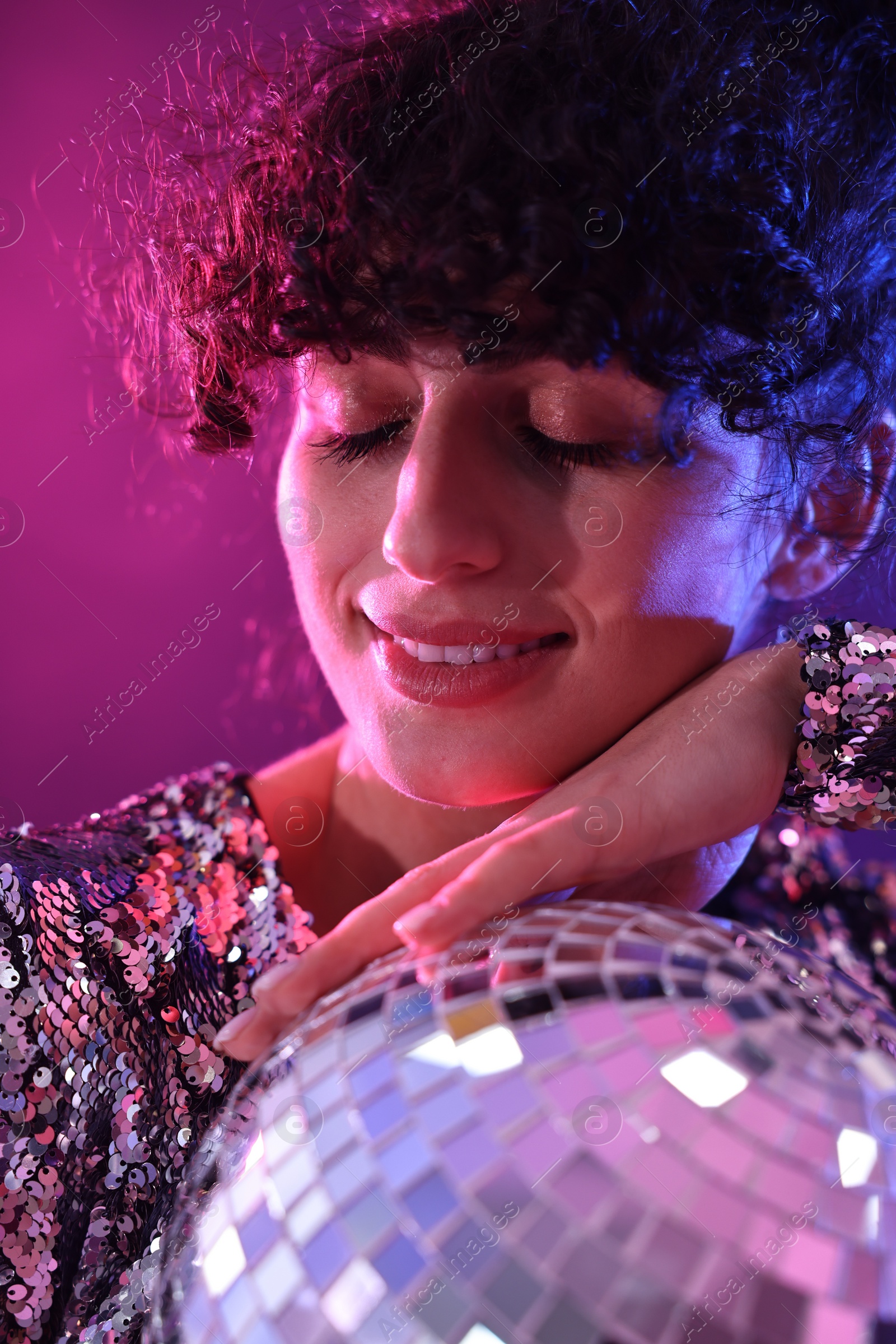 Photo of Beautiful young woman with disco ball posing on color background in neon lights, closeup