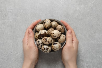 Photo of Woman holding bowl of quail eggs at light grey table, top view