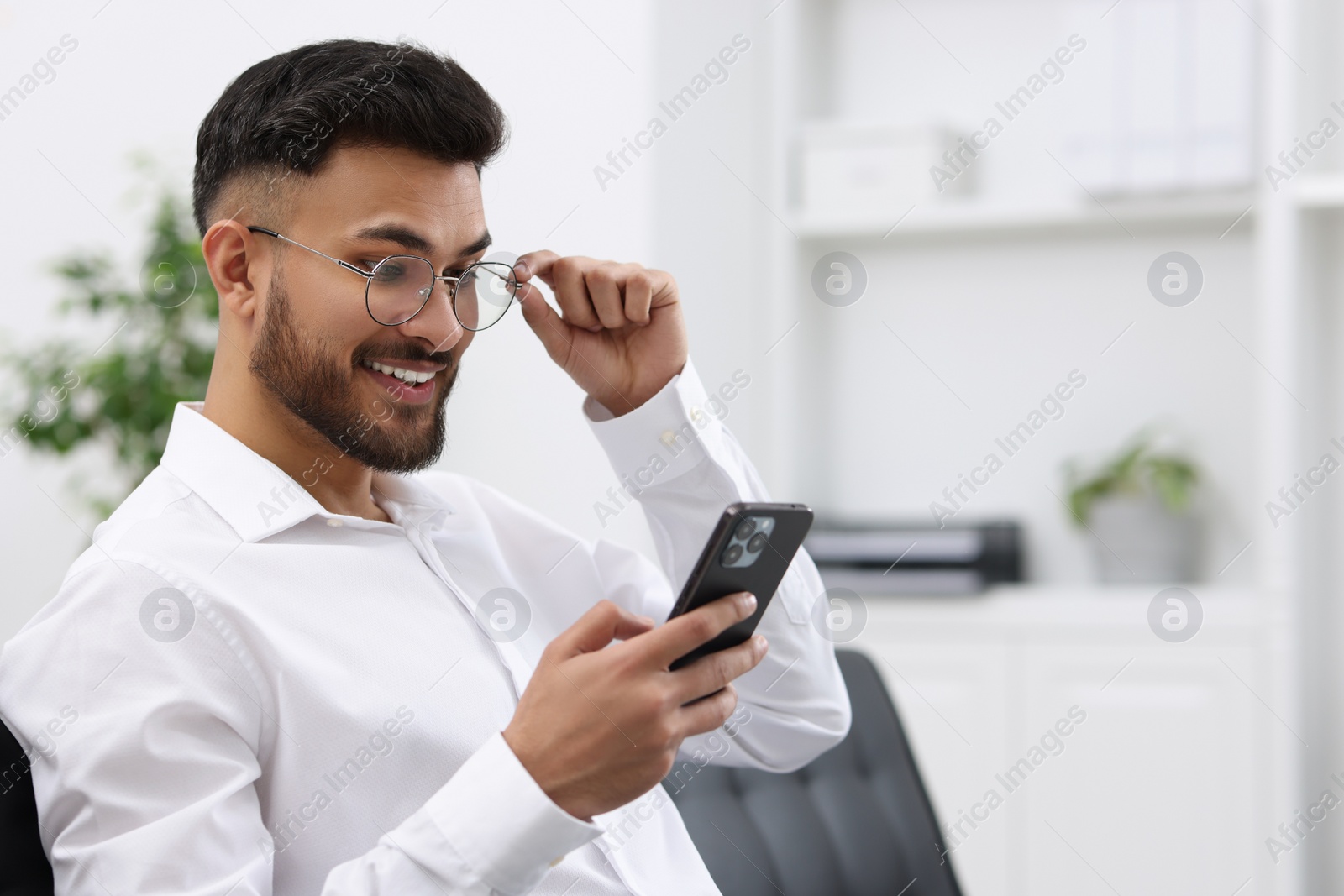 Photo of Happy young man using smartphone in office, space for text