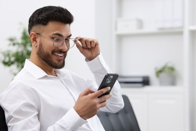 Happy young man using smartphone in office, space for text