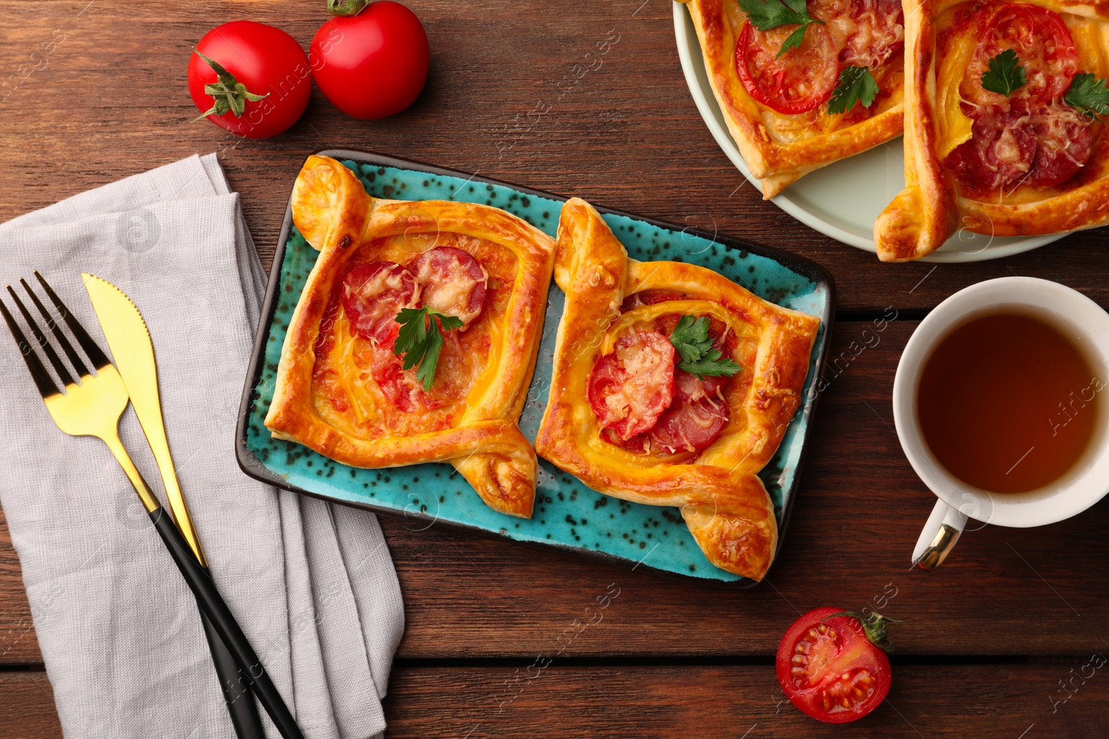 Photo of Fresh delicious puff pastry with cheese, tomatoes and parsley on wooden table, flat lay