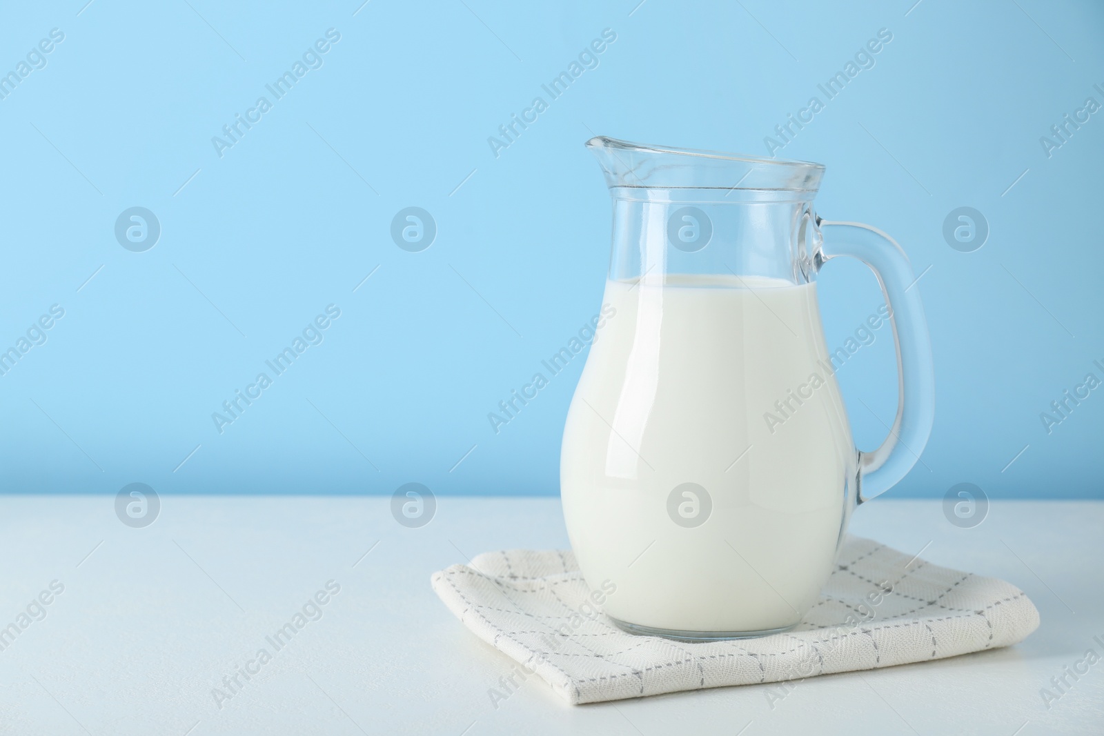 Photo of One jug of fresh milk on white table against light blue background, space for text