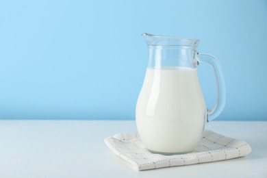 Photo of One jug of fresh milk on white table against light blue background, space for text