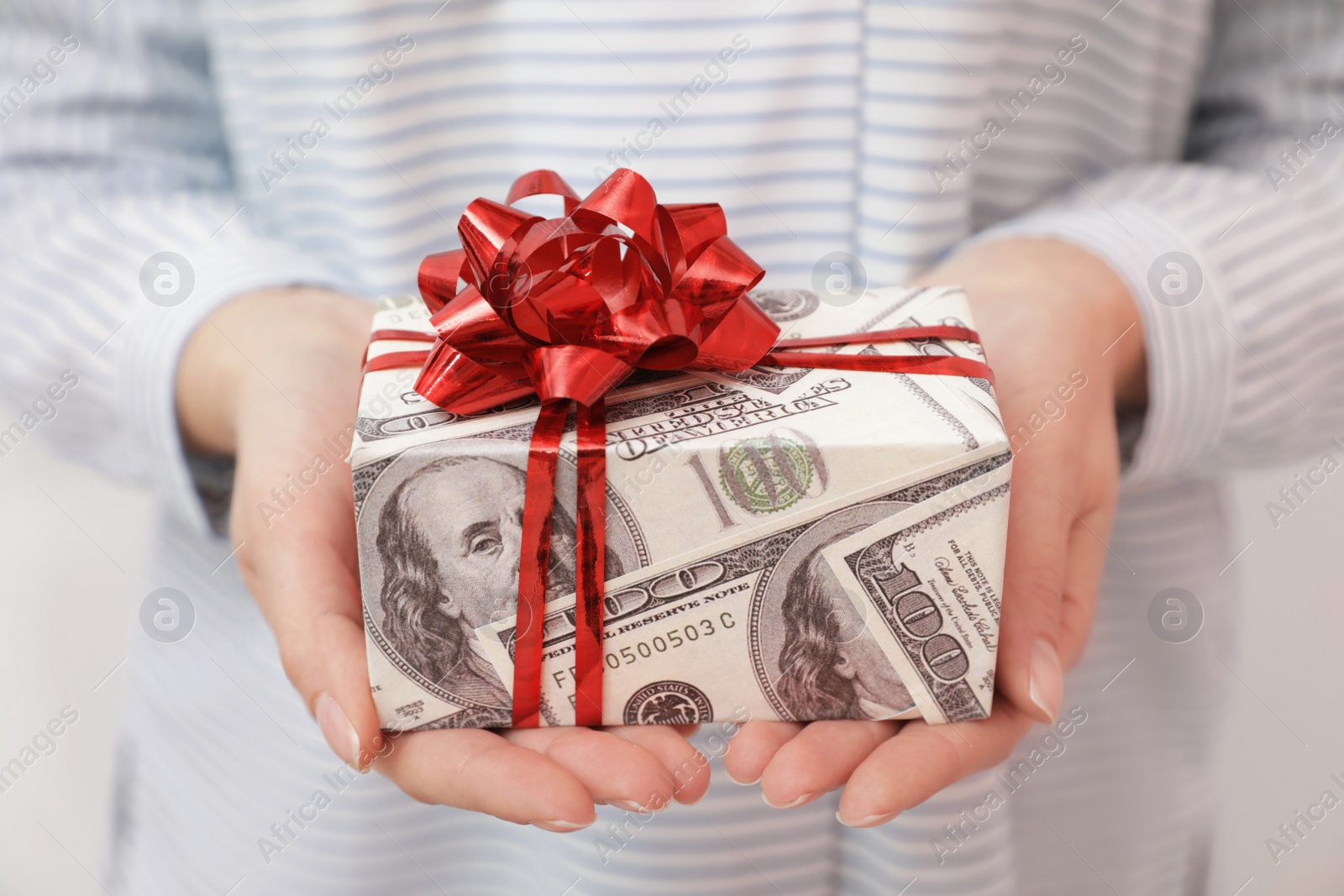 Photo of Woman holding gift box wrapped in dollars, closeup