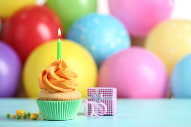 Photo of Delicious birthday cupcake with burning candle and gift on light blue wooden table. Space for text