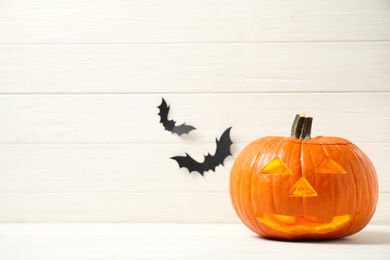 Photo of Scary jack o'lantern pumpkin on white wooden background, space for text. Halloween decor