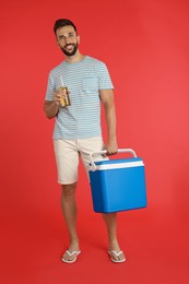 Photo of Happy man with cool box and bottle of beer on red background