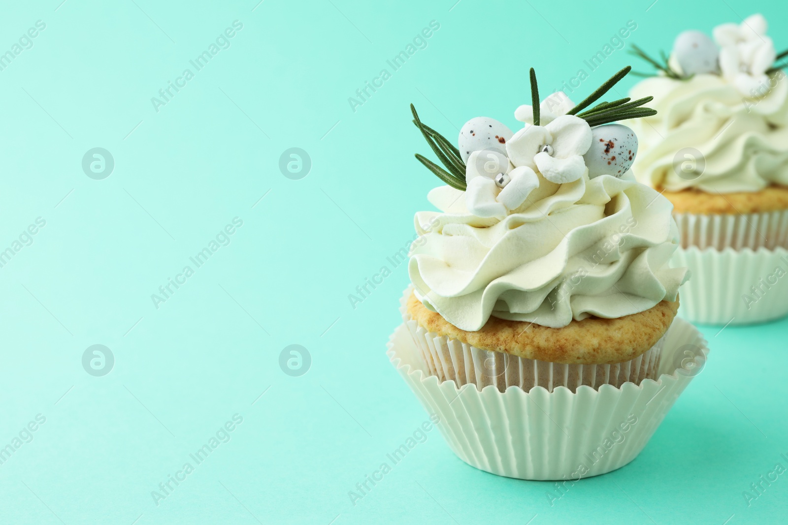 Photo of Tasty Easter cupcakes with vanilla cream on turquoise background, space for text