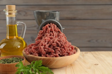 Photo of Mincing beef with manual meat grinder. Parsley, oil and spices on wooden table. Space for text