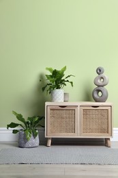 Photo of Wooden chest of drawers with decor and houseplants near light green wall indoors