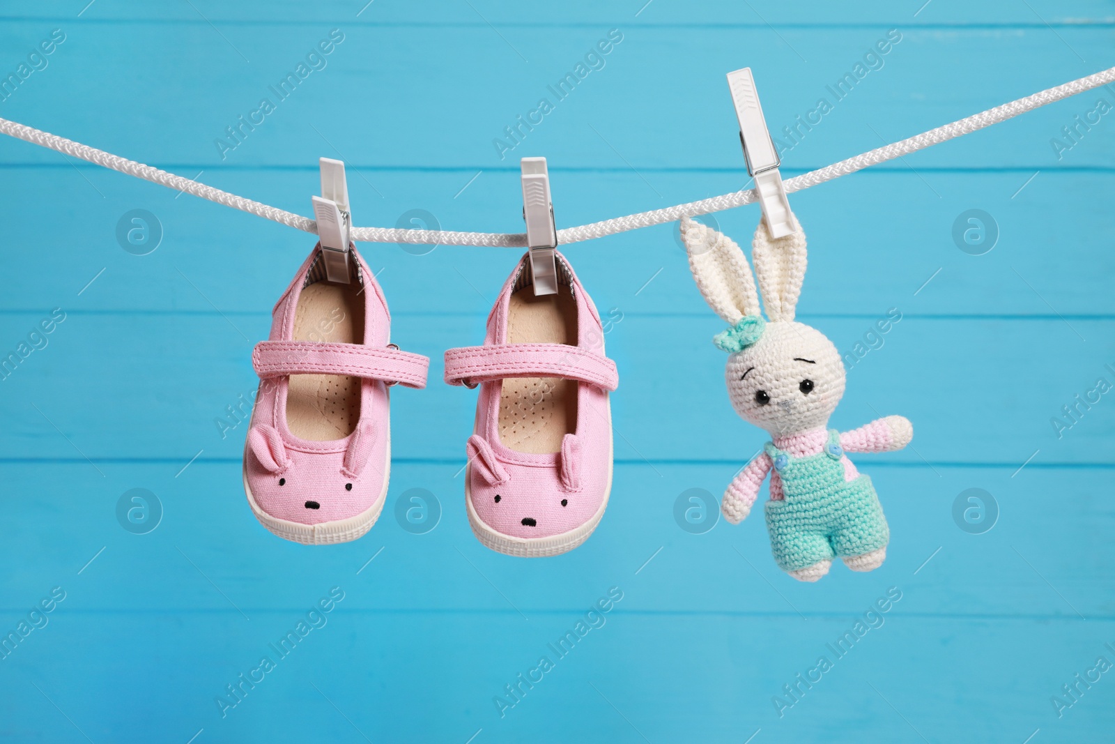 Photo of Cute baby shoes and crochet toy drying on washing line against light blue wooden wall