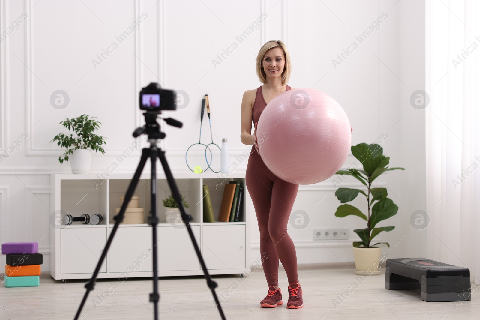 Photo of Smiling sports blogger holding fit ball while recording fitness lesson with camera at home