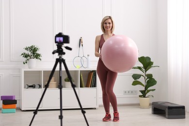 Photo of Smiling sports blogger holding fit ball while recording fitness lesson with camera at home