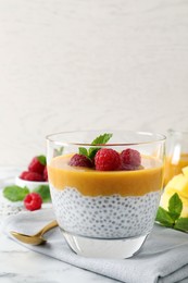 Photo of Delicious chia pudding with mango sauce and raspberries on white marble table