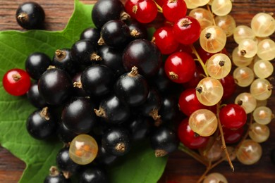 Photo of Different fresh ripe currants and green leaf on wooden table, closeup