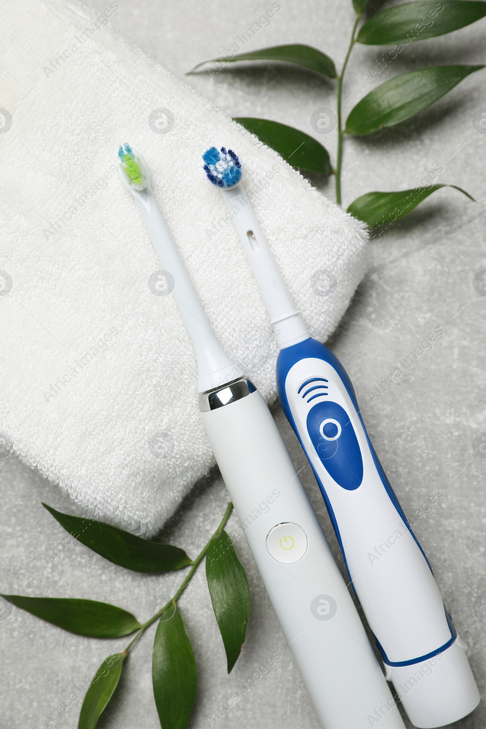 Photo of Electric toothbrushes, towel and leaves on grey textured table, flat lay