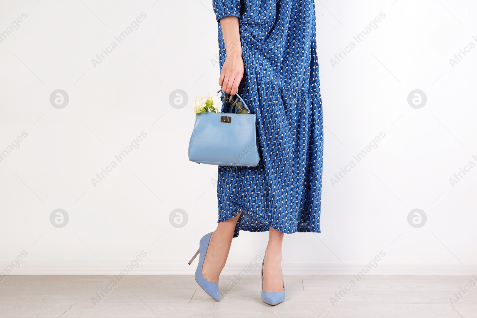 Photo of Stylish woman with handbag and spring flowers near light wall