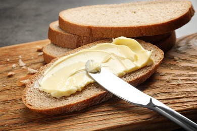 Photo of Spreading butter onto toast with knife on wooden board