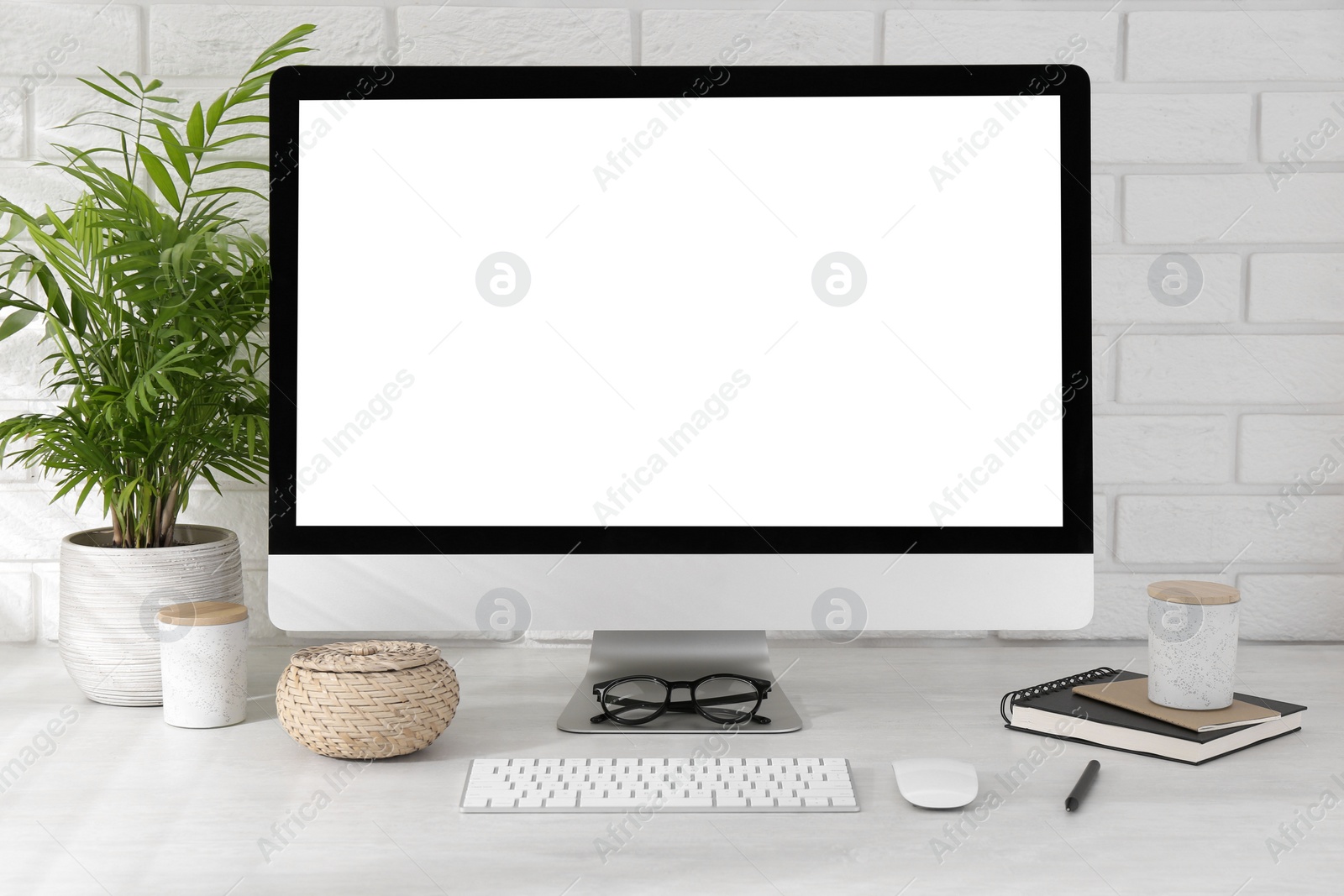 Photo of Office workplace with computer, glasses, stationery and houseplant on light table near white brick wall