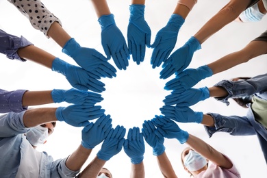 Photo of People in blue medical gloves joining hands on light background, low angle view