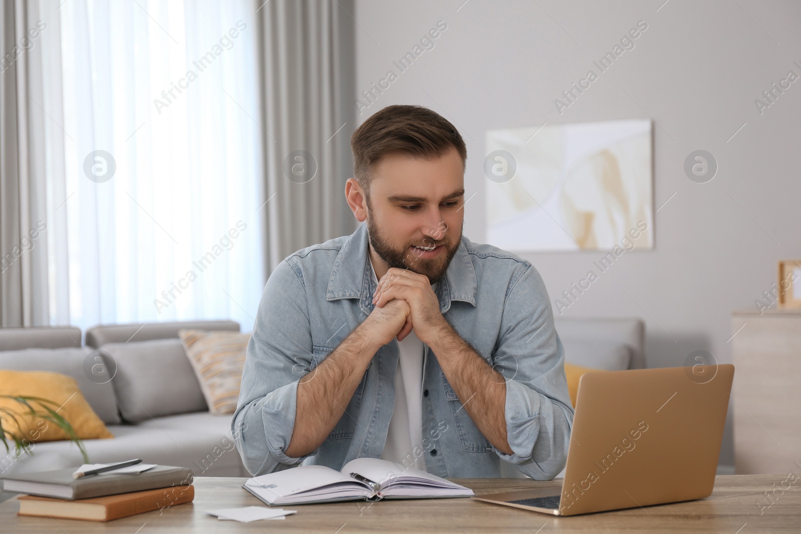 Photo of Young man watching online webinar at table indoors