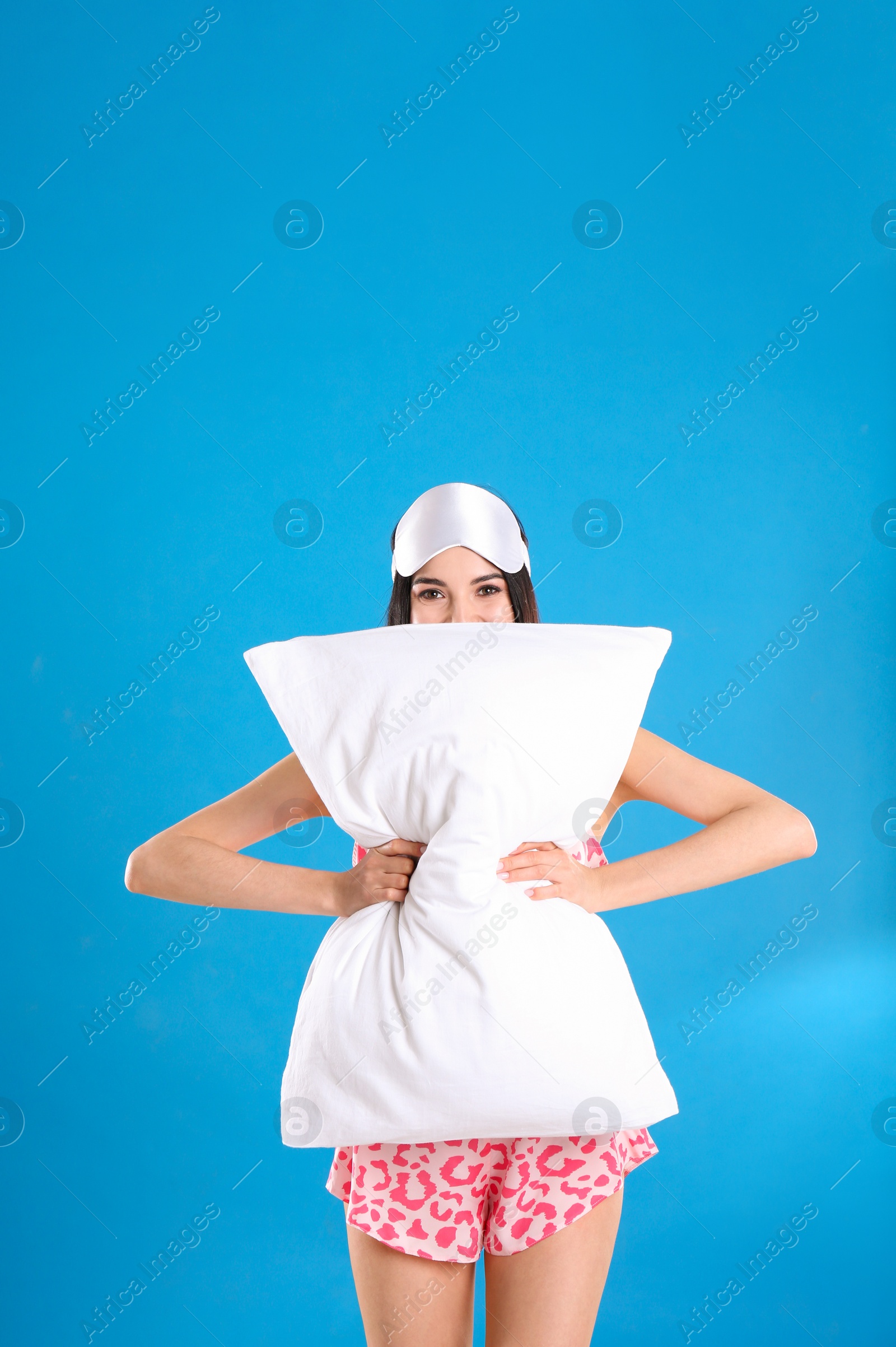 Photo of Young woman with pillow and sleep mask on blue background