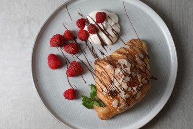 Delicious croissant with raspberries, cream and chocolate on grey table, top view