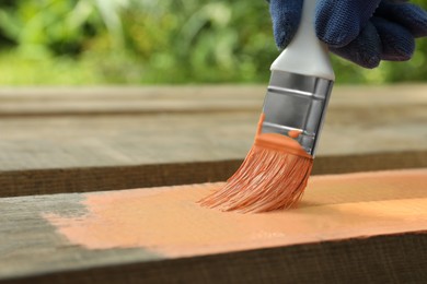 Worker painting wooden surface with coral dye outdoors, closeup. Space for text