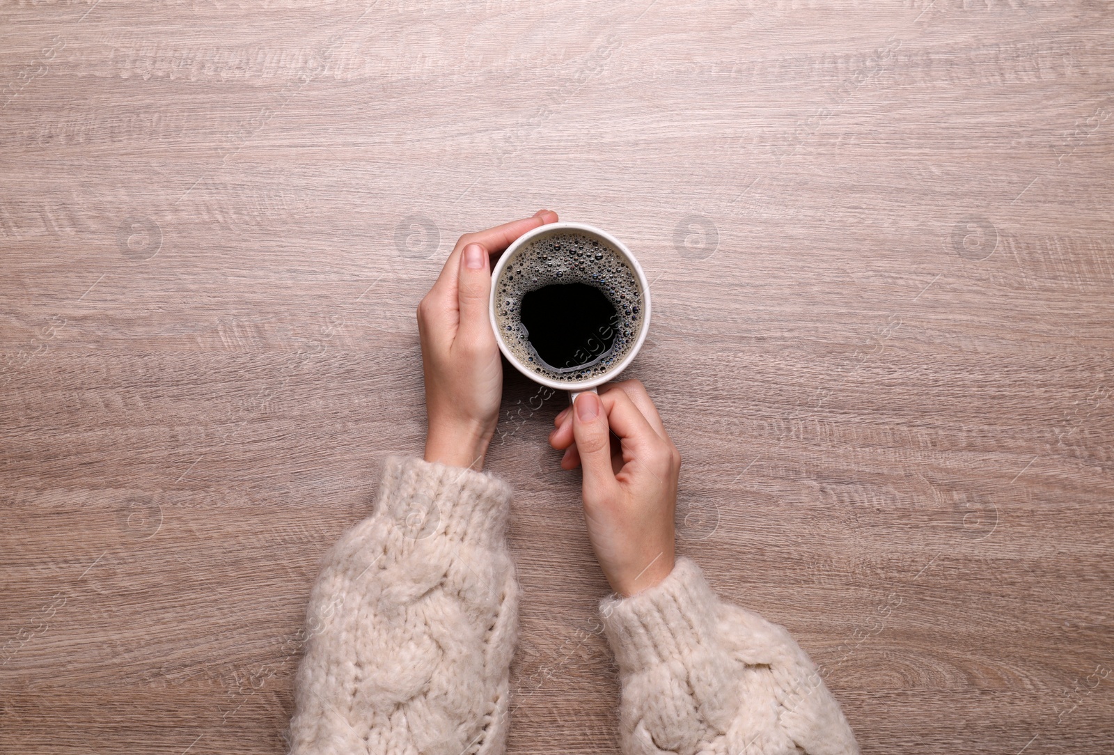 Photo of Woman with cup of coffee at wooden table, top view