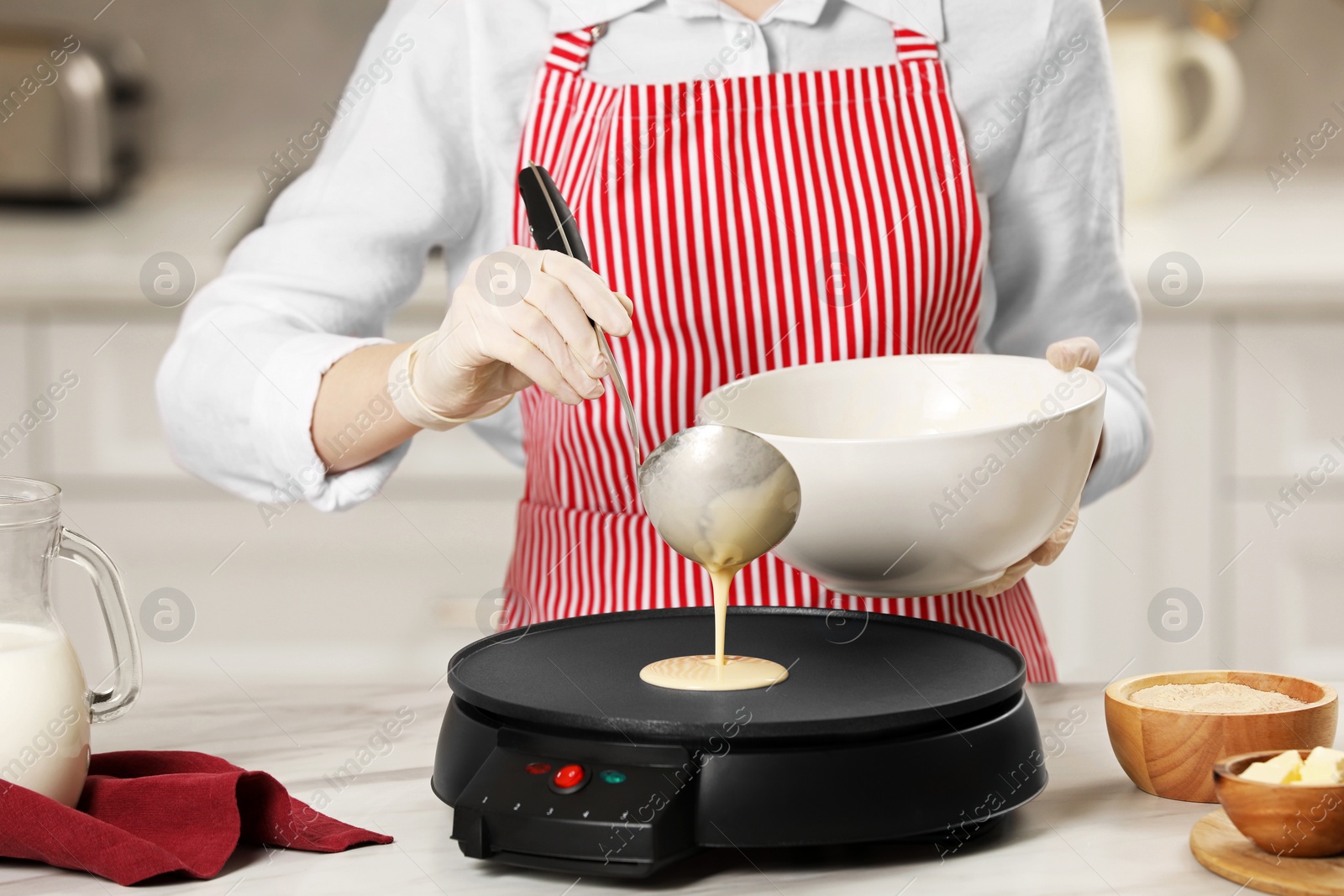 Photo of Woman cooking delicious crepe on electric pancake maker at white marble table in kitchen, closeup