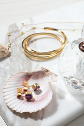 Photo of Different elegant bijouterie, shells and bottle of perfume on white table, closeup