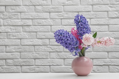 Photo of Beautiful hyacinths in pink vase on table against brick wall, space for text. Spring flowers