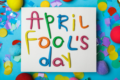 Photo of Paper note with phrase APRIL FOOL'S DAY and decor on light blue background, flat lay