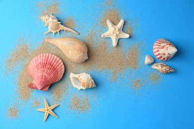 Photo of Beautiful starfishes, shells and sand on blue background, flat lay