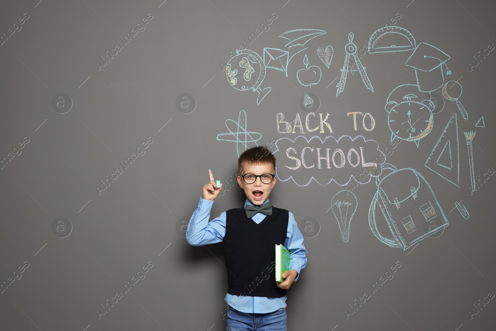 Photo of Little child in uniform near drawings with text BACK TO SCHOOL on grey background