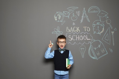 Little child in uniform near drawings with text BACK TO SCHOOL on grey background